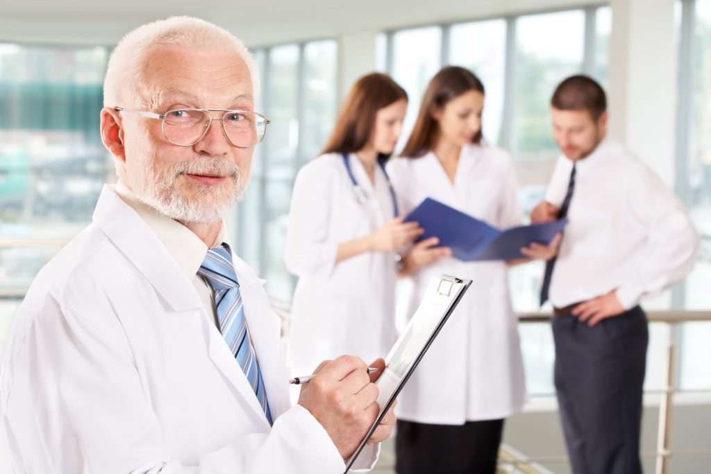 A portrait of doctor with two attractive nurses and patient in the background